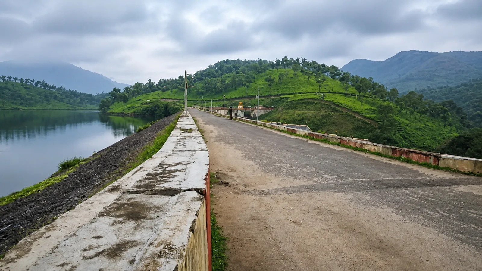 Road across Anayirangal Dam beside a calm reservoir and green hills near Pooppara
