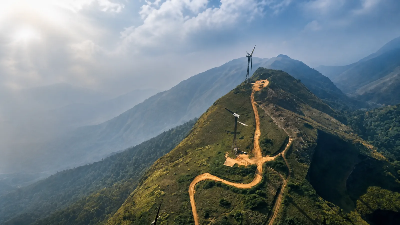 Wind turbines and a winding dirt road along the misty Chathurangappara mountain ridge