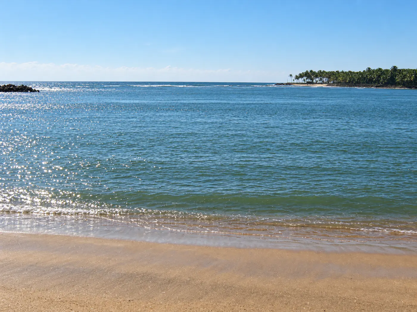 A calm estuary opening towards the sea with coconut palms along the distant shore