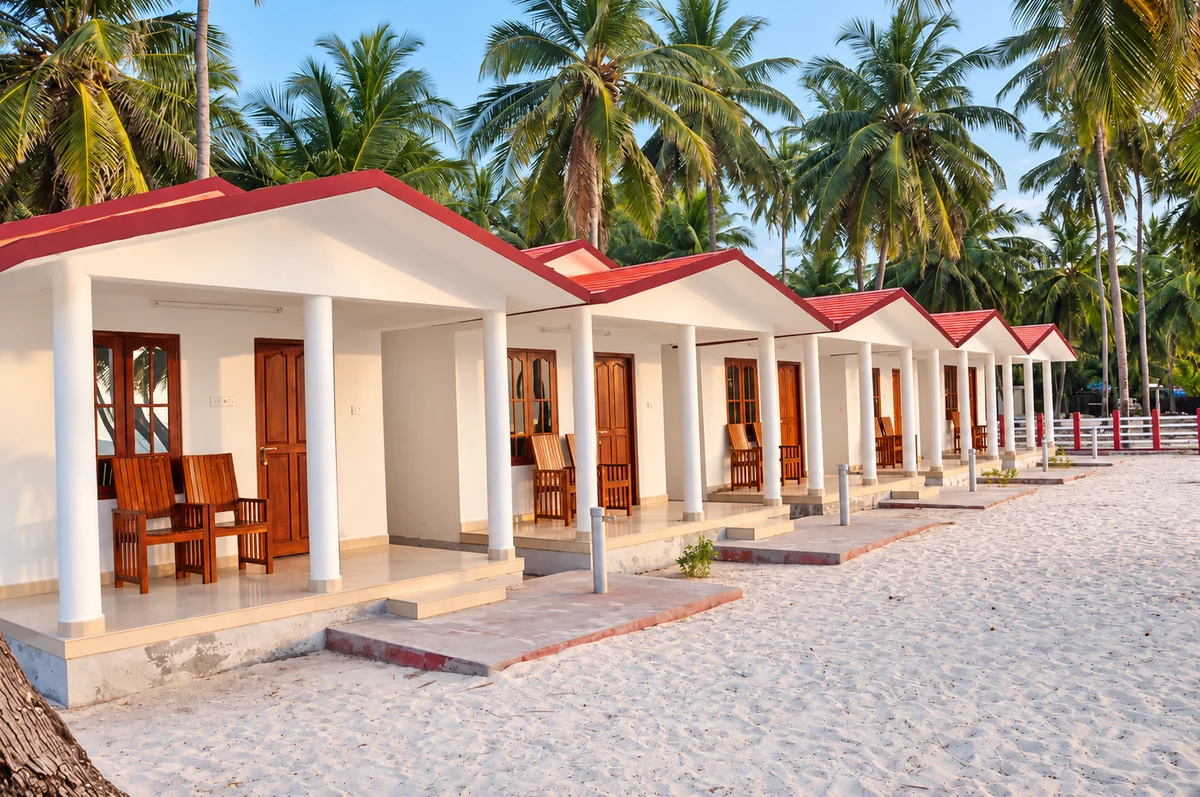 Supplied photo of white island cottages with red roofs, shaded porches and coconut palms, enhanced for lighting and clarity