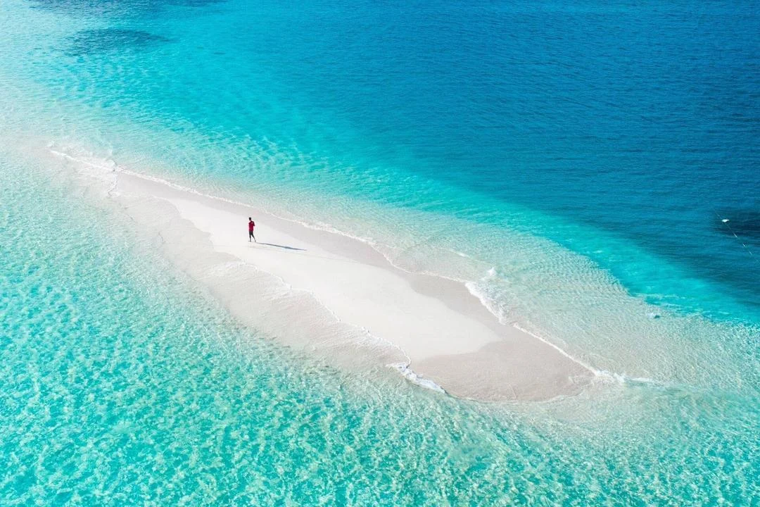 An aerial view of a white sandbank surrounded by clear turquoise water